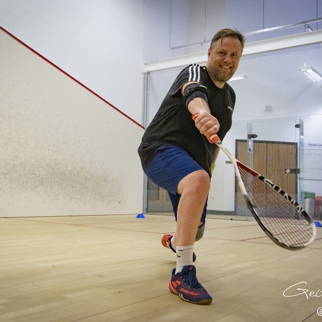 Squash player smiling for the camera as he plays his shot.